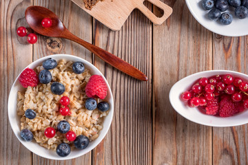 Top view of porridge with blueberries and raspberries on wooden background. Vegan breakfast.