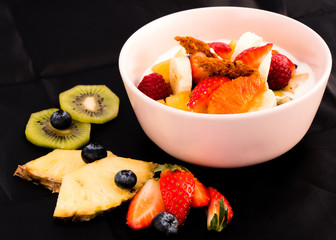 weißer Joghurtbecher mit Früchten vor schwarzem Hintergrund