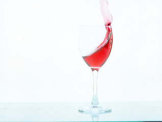 Red wine pouring in glass goblet isolated on white background