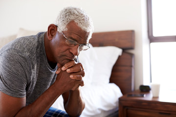 Depressed Senior Man Looking Unhappy Sitting On Side Of Bed At Home With Head In Hands - Powered by Adobe