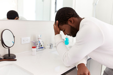 Depressed Man Leaning On Sink In Bathroom With Head In Hands
