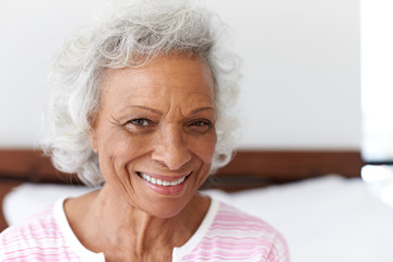 Head And Shoulders Portrait Of Smiling Senior Woman Sitting On Bed At Home Looking Positive