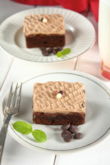 Chocolate bakery style cake brownie  with chocolate cream on top on a white plate and mint leaf and a glass of milk in the background
