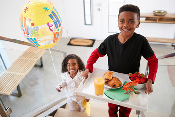 Portrait Of Children Bringing Parents Breakfast In Bed On Tray With Balloon To Celebrate Birthday