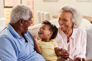 Foto op Canvas Grandparents Sitting On Sofa At Home Playing With Baby Granddaughter © Monkey Business