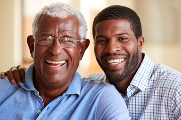 Portrait Of Smiling Senior Father Being Hugged By Adult Son At Home