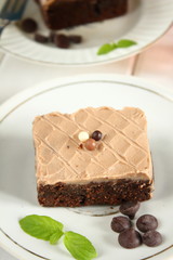 Chocolate bakery style cake brownie  with chocolate cream on top on a white plate and mint leaf and a glass of milk in the background