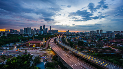 Naklejka na ściany i meble Kuala Lumpur city skyline during dramatic sunset with elevated highway leading into the city.