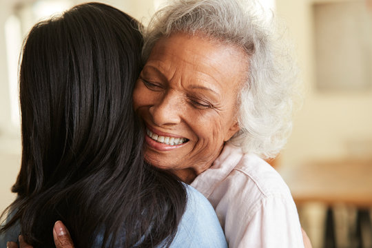 Over The Shoulder View Of Senior Mother Being Hugged By Adult Daughter At Home