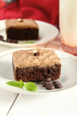 Chocolate bakery style cake brownie  with chocolate cream on top on a white plate and mint leaf and a glass of milk in the background