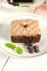 Chocolate cake brownie brownie with chocolate cream on top on a white plate and mint leaf and a glass of milk in the background