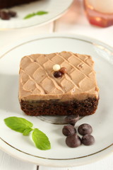 Chocolate bakery style cake brownie  with chocolate cream on top on a white plate and mint leaf and a glass of milk in the background