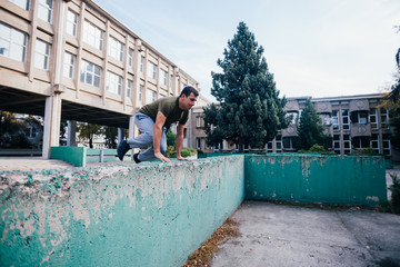 Strongman while training parkour jumping over the concrete wall at an urban area.
