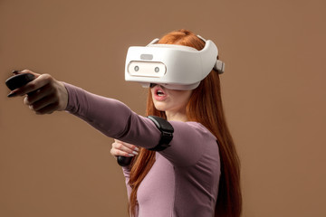 Casual ginger-haired woman in purple pullower wearing VR headset and looking involved in 3D...