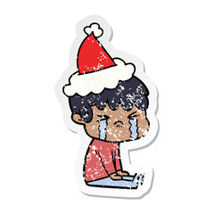 distressed sticker cartoon of a boy crying wearing santa hat