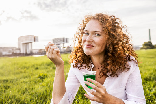 Germany, Cologne, portrait of happy young woman eating jelly on meadow