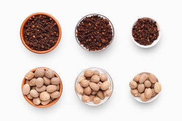 Different sized bowls with cloves and nutmeg on white