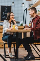 attractive woman with glass of juice and handsome man with cup of coffe sitting at table in coffee house
