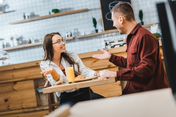 selective focus of attractive brunette woman with glass of juice and handsome man with cup of coffe sitting and smiling at table in coffee house