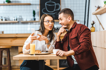 attractive brunette woman and handsome man sitting at table and looking to smartphone in coffee house