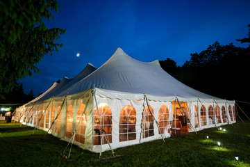 A wedding tent at night with blue sky and the moon. The walls are down and the tent is set up on a...