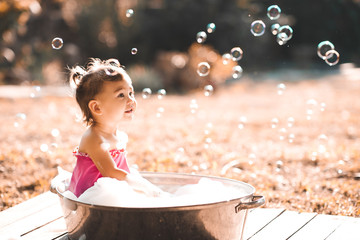 Cute bby girl 1-2 year old having bath with soap bubbles outdoors close up. Summer time. Childhood.