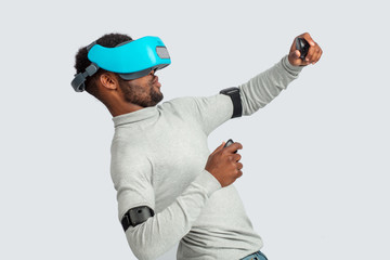 Studio shot of athletic man in white casual clothes fighting, making a punch to his virtual opponent using wearable virtual reality headset.