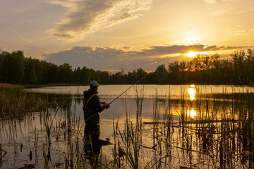 angler standing in a lake and catching the fish at sunset