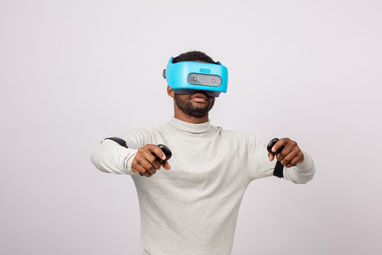 Dark skinned ethnic man using virtual reality glasses watching a simulation image 3D, holding gamepads in raised hands as if he plays Car Race