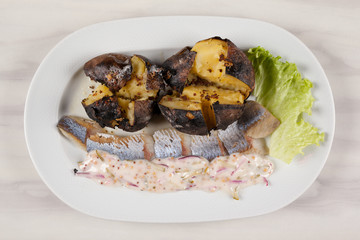 Baked potatoes and herring with sauce and salad on a white plate.