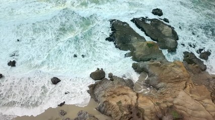 Straight down aerial view of waves crashing against the rocks on the California coast.