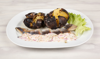 Baked potatoes and herring with sauce and salad on a white plate.