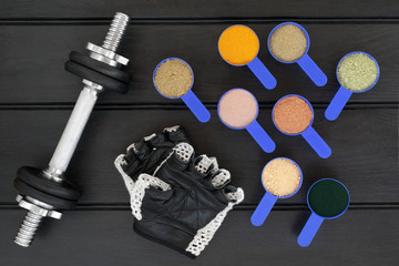 Body building dumbbell weights and gloves with dietary food supplement powders. Top view on wood table.