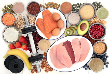 Body building health food and dumbbell weights with high protein meat, fish, nuts, seeds, legumes, grains, dairy, dietary supplement powders, multi vitamin & chlorella tablets, vegetables and fruit.