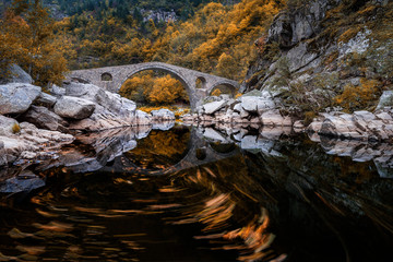 Devil's bridge, Bulgaria. Ancient stone bridge over Arda river, autumn time with leaves in water. Rhodope mountain