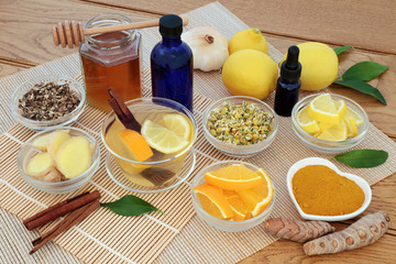 Herbal medicine for flu and cold remedy with honey, orange and lemon drink, essential oils and a selection of herbs and spices on bamboo and oak background.