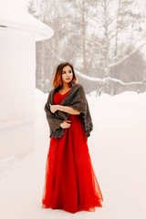 Beautiful girl in a long dress and a woolen shawl on her shoulders in the winter on the street near...