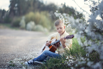 Handsome teen with guitar sitting on grass in the park.