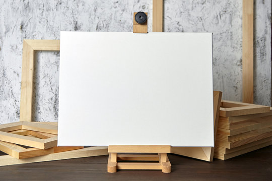 White blank cotton canvas for acrylic and oil paints, a wooden easel and stretcher bars on table
