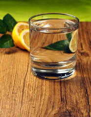 glass cup of water with lemon on wooden table and dark background
