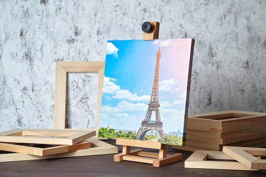 Photo of Paris printed on canvas, a wooden easel and stretcher bars on table