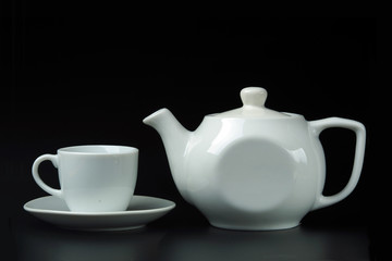 White teapot and white cup on a white saucer on a black background