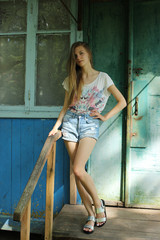Young, slim girl posing on the threshold of a vintage house, on the background of the old door in...