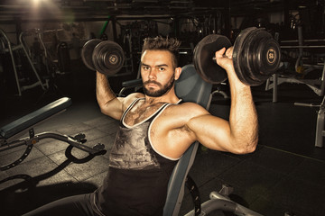 Fototapeta na wymiar Handsome young athletic man lifting weights at the gym studio