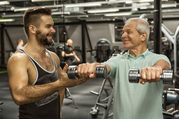 Professional fitness trainer helping his senior client exercising with dumbbells