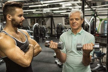 Professional fitness trainer helping his senior client exercising with dumbbells