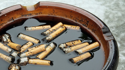 Filthy ashtray filled with cigarette butts in black water