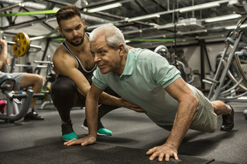 Fototapeta na wymiar Senior man doing pushups with his personal trainer at the gym