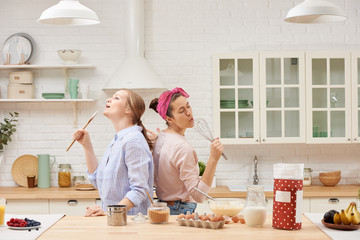 Two cheerful friends cook together desserts and sing