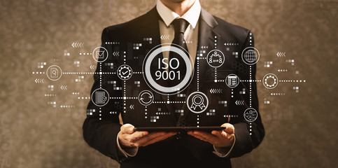 ISO 9001 with businessman holding a tablet computer on a dark vintage background